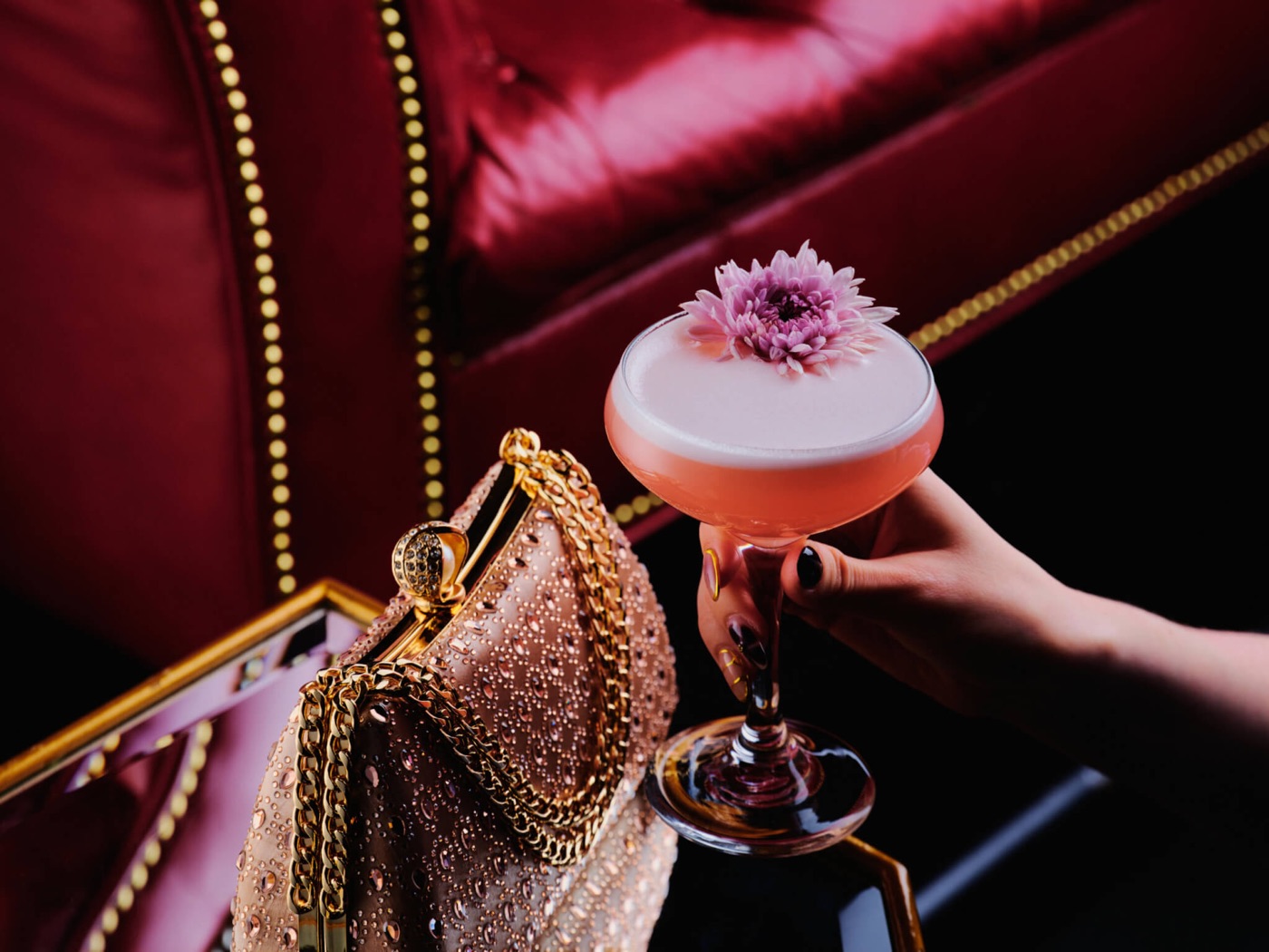 A signature Beauty & Essex cocktail garnished with a flower beside a jeweled clutch